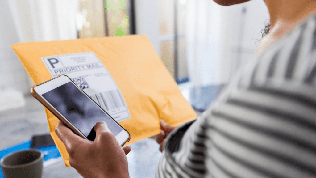 Person holding an envelope with shipping labels, checking shipping tracking information on their phone